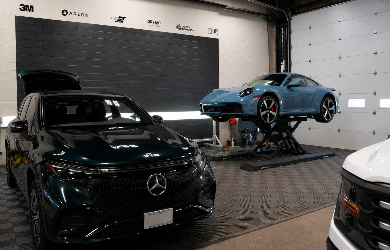 Mercedes EQS and a Porsche 911 on the lift in the Auto Trim Design install bay